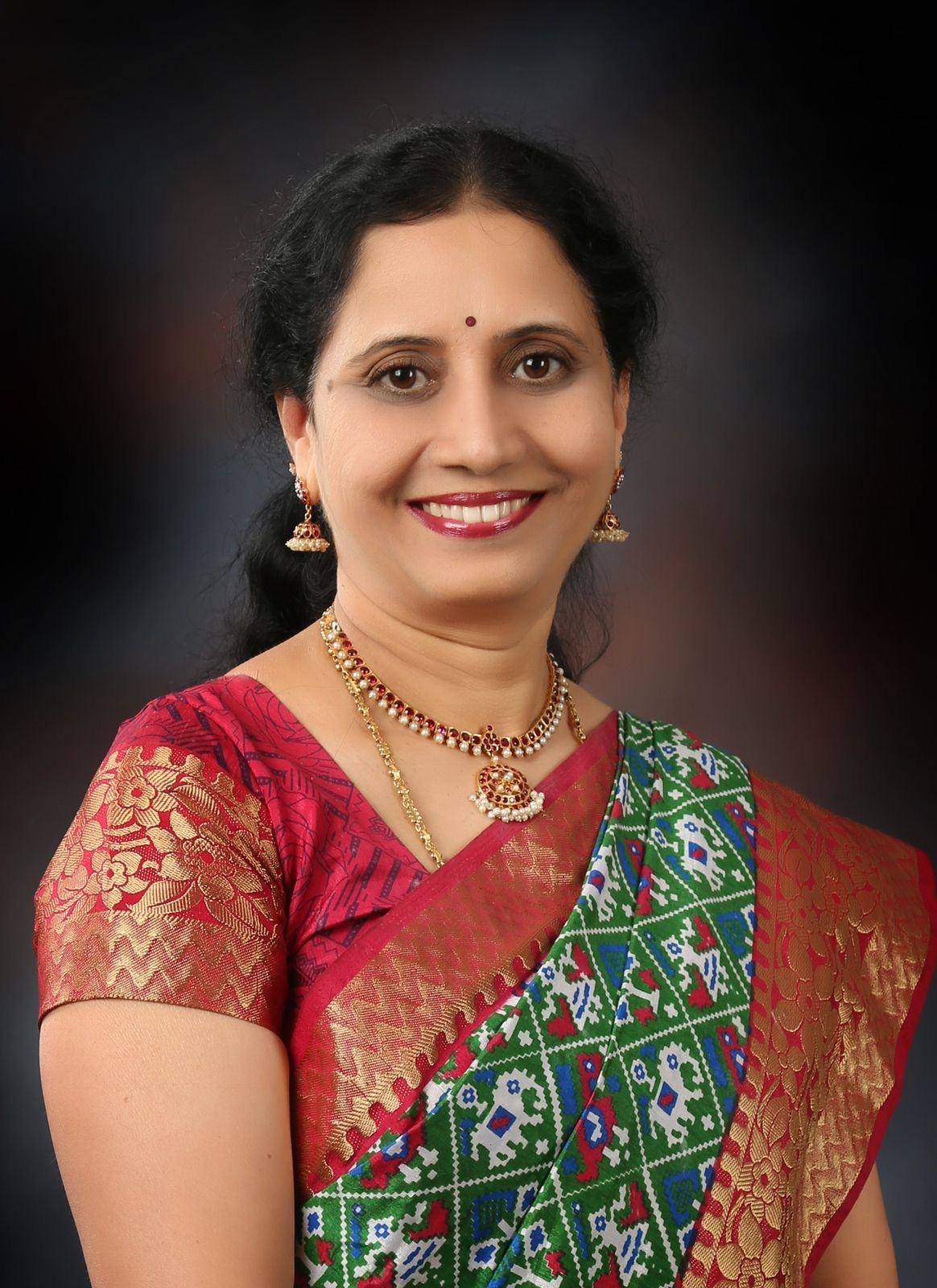 Studio portrait of Dr. P. Lakshmi Satish in a red and gold saree.